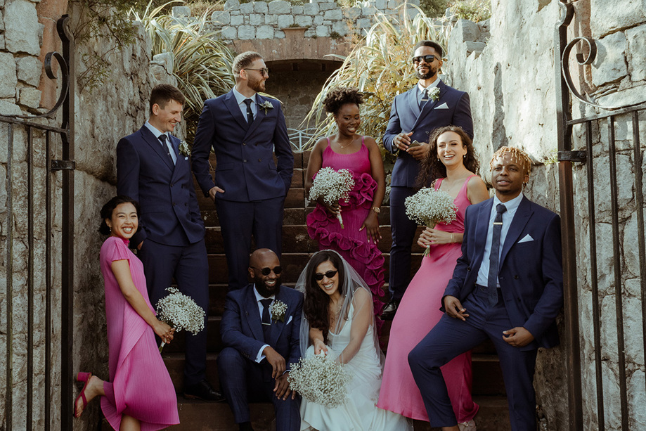 Bridal party wearing pink and groomsmen wearing navy with the married couple who are laughing and wearing sunglasses