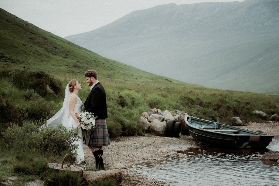 Bride and groom looking at each other down by the water with boat beside them