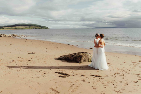 Two brides embrace in a kiss on a sandy beach