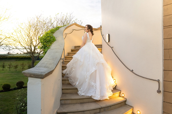 Bride smiles and shows off her dress on staircase with rope handle