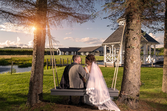 Bride and groom sit on swing looking at each other, with brides veil flowing behind her