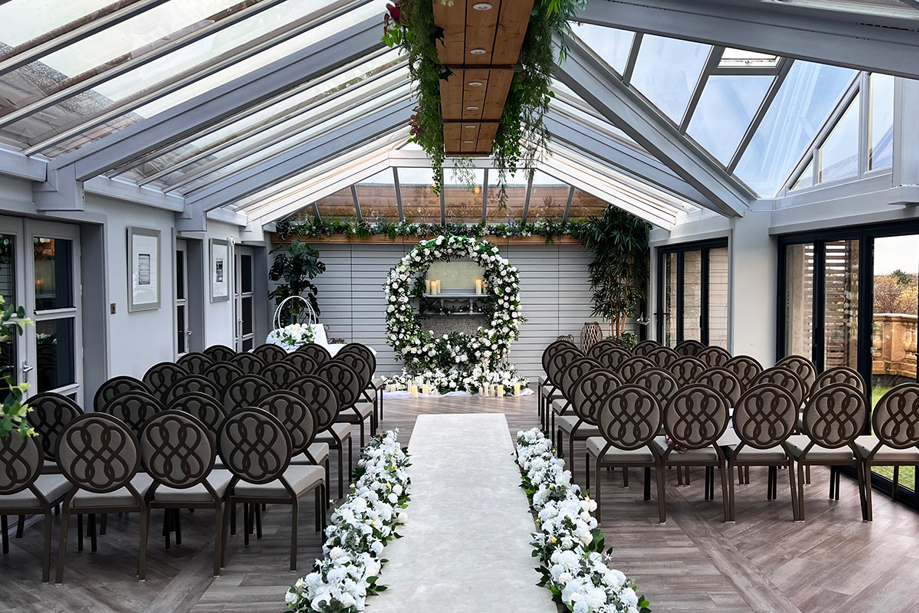 Ceremony room with aisle lined with white flowers and circular floral arch with candles at altar
