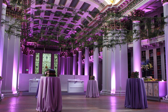 Purple-hued room with streams of leaves above dancefloor with four tables for drinks