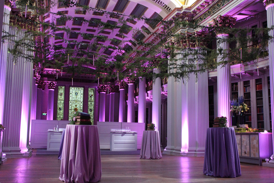 Purple-hued room with streams of leaves above dancefloor with four tables for drinks