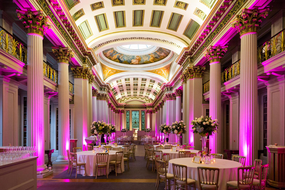 Pink-hued main room set up for meal with grand Corinthian columns and regal interior