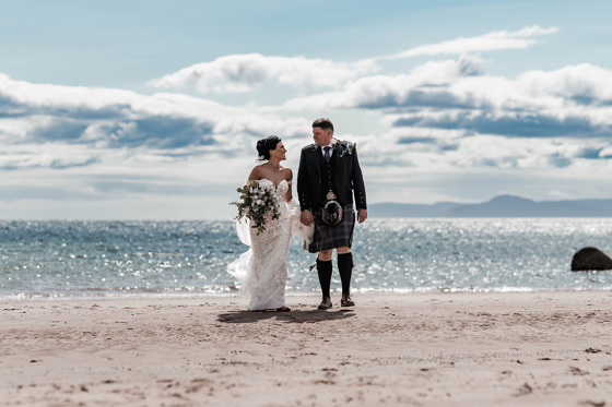 Bride and groom walk across beach in front of The Waterside Hotel