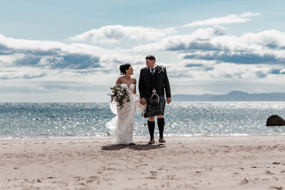 Bride and groom walk across beach in front of The Waterside Hotel