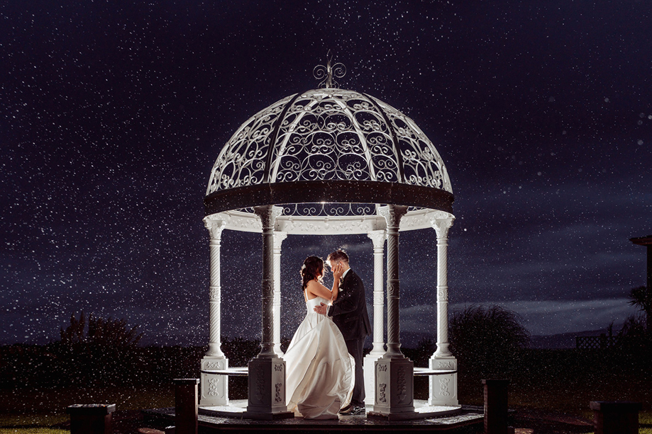 Starry sky image of a bride and groom embracing beneath white wedding bandstand in the private gardens of The Waterside Hotel