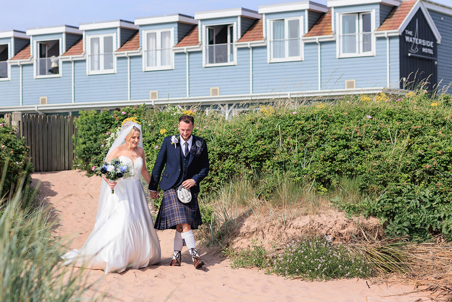 Bride and groom walking on to beach from The Waterside Hotel