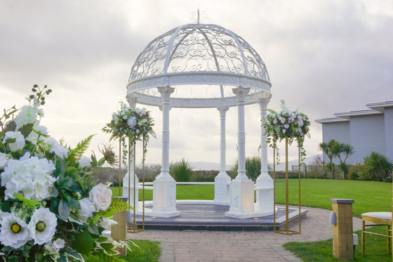 Cloudy day image of white wedding bandstand with flowers in foreground