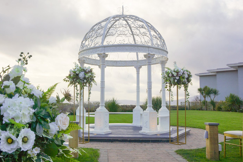 Cloudy day image of white wedding bandstand with flowers in foreground