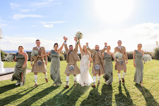 Wedding party walk together across grass on sunny wedding day at The Waterside Hotel