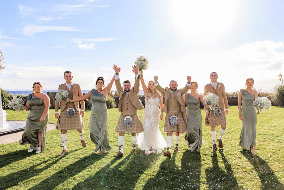 Wedding party walk together across grass on sunny wedding day at The Waterside Hotel