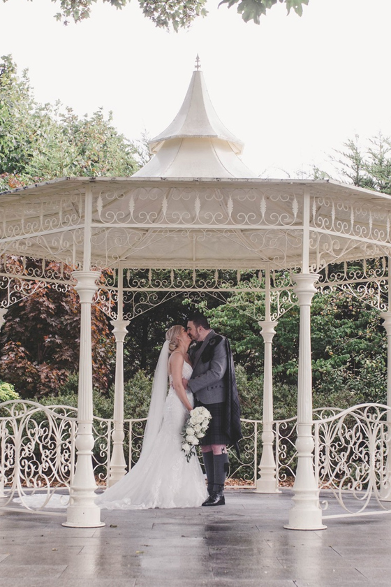 Bride and groom kiss beneath white bandstand at Carlton Hotel in Prestwick
