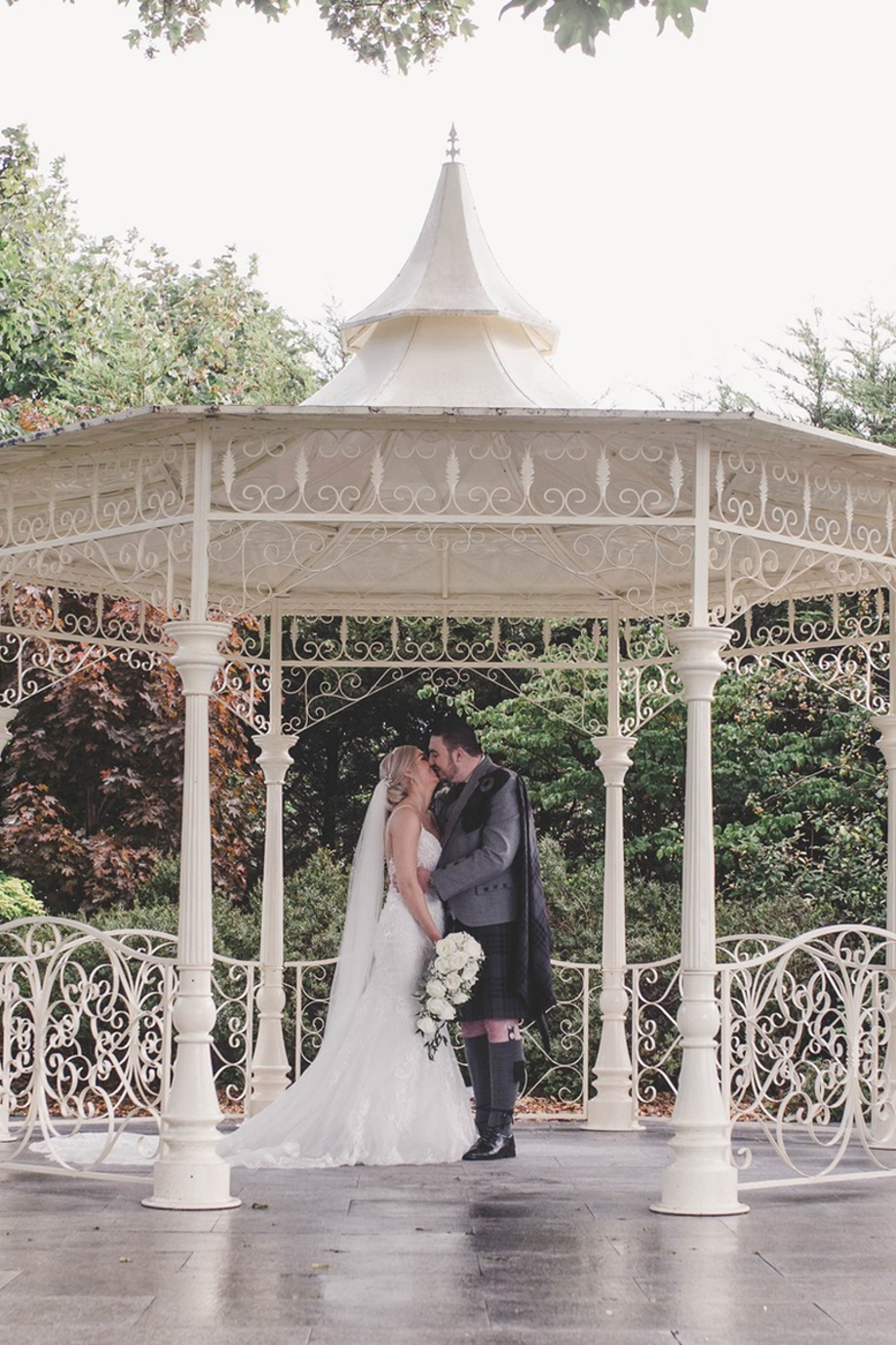 Bride and groom kiss beneath white bandstand at Carlton Hotel in Prestwick