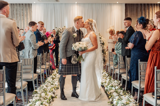 Bride and groom kiss as they walk back up aisle as guests clap at the Carlton Hotel in Prestwick