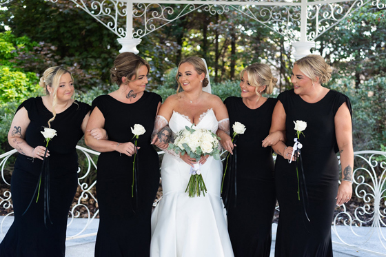 Bride and her bridesmaids wearing black, each holding one white rose