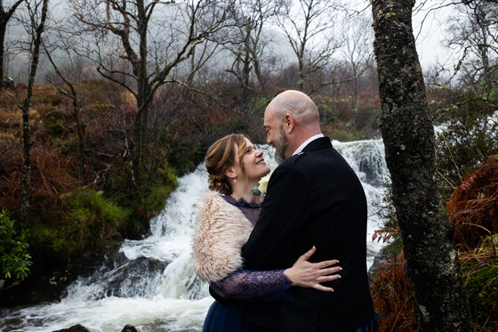 Wedding couple embracing beside a waterfall near Castle Craigard