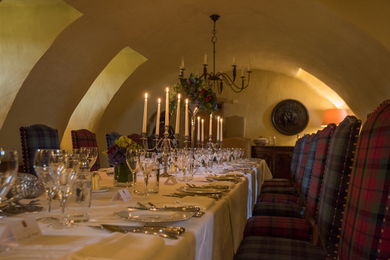 Candlelit wedding dining table with long wooden table, silver candlesticks and tartan chairs at Fenton Tower