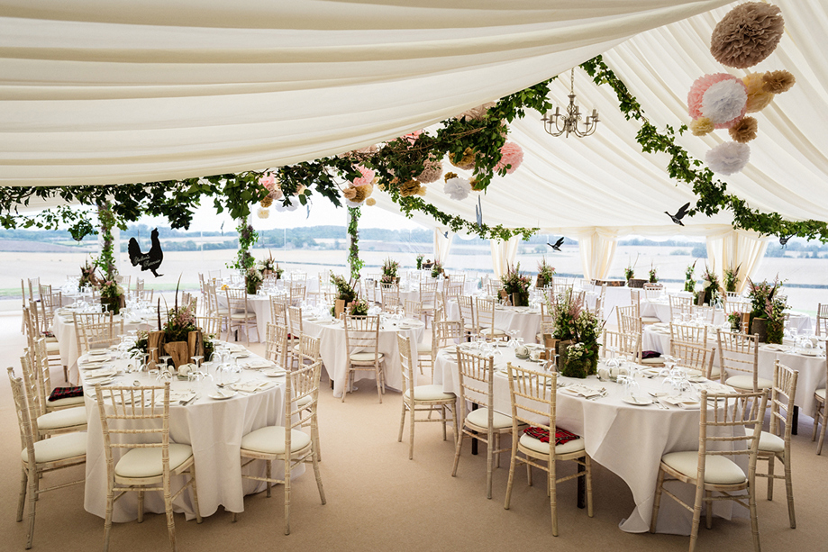 Wedding marquee reception with round tables, white linen and floral styling overlooking the East Lothian countryside at Fenton Tower