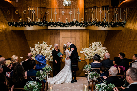 Bride and groom kiss at altar in the Ballroom on board Fingal Hotel in Edinburgh while guests clap.