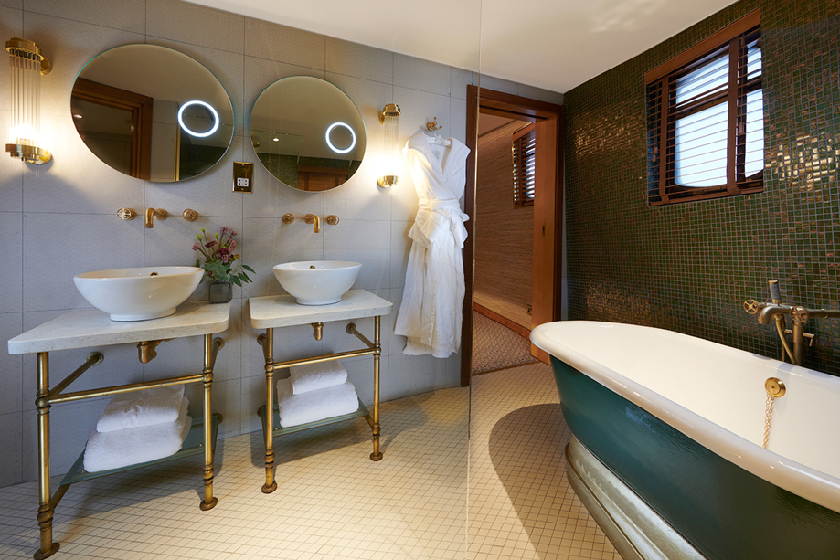 Skerryvore Suite bathroom with double sink and teal bath with gold accents throughout.