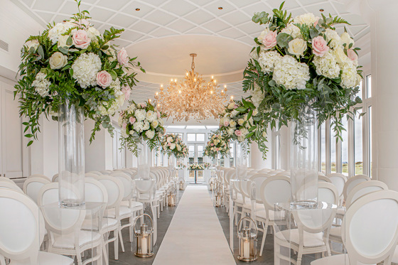 Aisle decorated with large bouquets of pink on each side and white flowers and candle lanterns