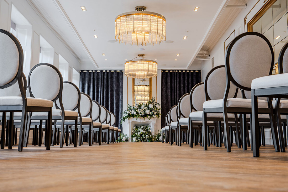 Aisle view of the Ceremony Room at The Exchange in Glasgow, showing a large floral display at the altar and chandeliers.