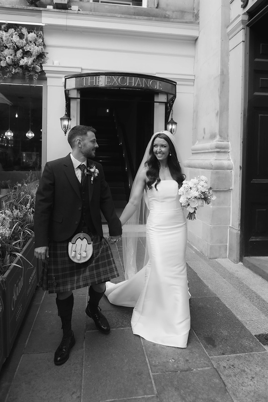 Black and white image of a bride and groom leaving The Exchange in Glasgow holding hands.