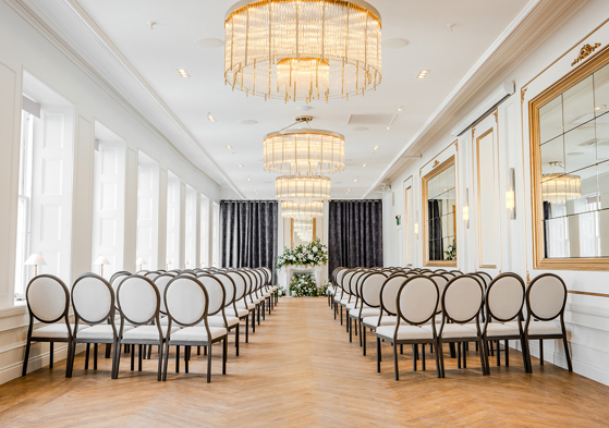 The Exchange wedding venue in Glasgow's ceremony room, with chandeliers, mirrors on walls and floral display at altar.