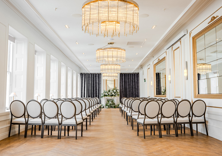 The Exchange wedding venue in Glasgow's ceremony room, with chandeliers, mirrors on walls and floral display at altar.