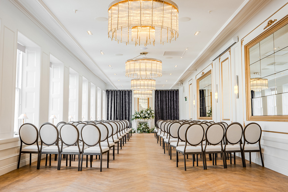 The Exchange wedding venue in Glasgow's ceremony room, with chandeliers, mirrors on walls and floral display at altar.
