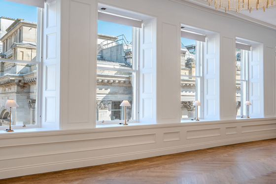 The large windows in the Ceremony Room at The Exchange, with small gold and white table lamps on each window ledge.
