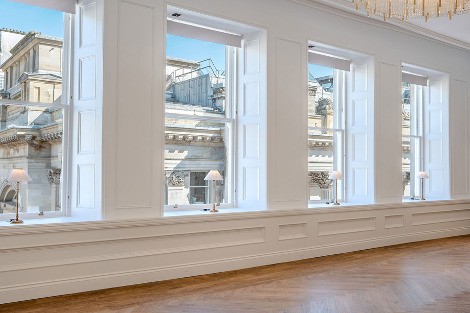 The large windows in the Ceremony Room at The Exchange, with small gold and white table lamps on each window ledge.