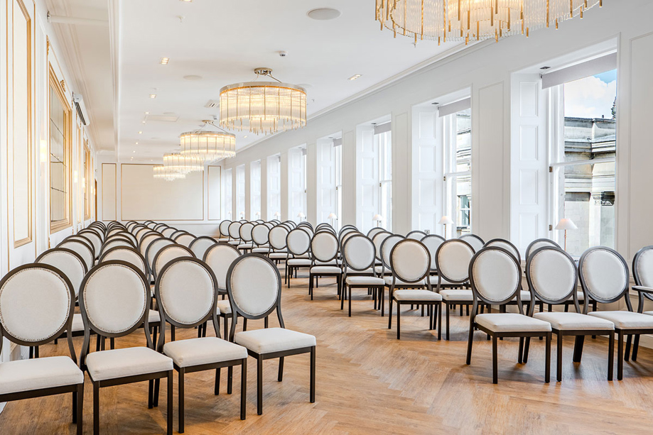 View of the Ceremony Room at The Exchange in Glasgow from the altar, displaying its stunning beige and dark wood chairs and chandeliers.