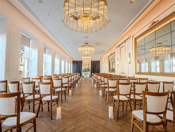 The Exchange wedding venue in Glasgow's ceremony room, with chandeliers, mirrors on walls and floral display at altar.