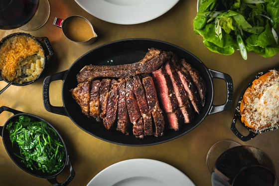 Sliced prime XL rib in a cast-iron pan at Hawksmoor Edinburgh, accompanied by greens, mac and cheese, and other signature sides.