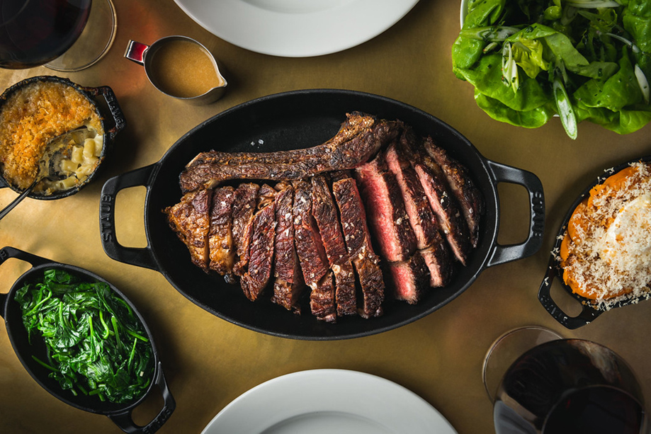 Sliced prime XL rib in a cast-iron pan at Hawksmoor Edinburgh, accompanied by greens, mac and cheese, and other signature sides.