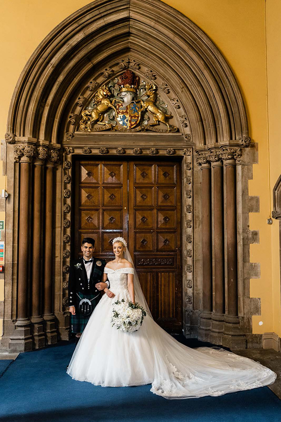 Bride and groom stand together outside the doors of the Memorial Chapel at the University of Glasgow.