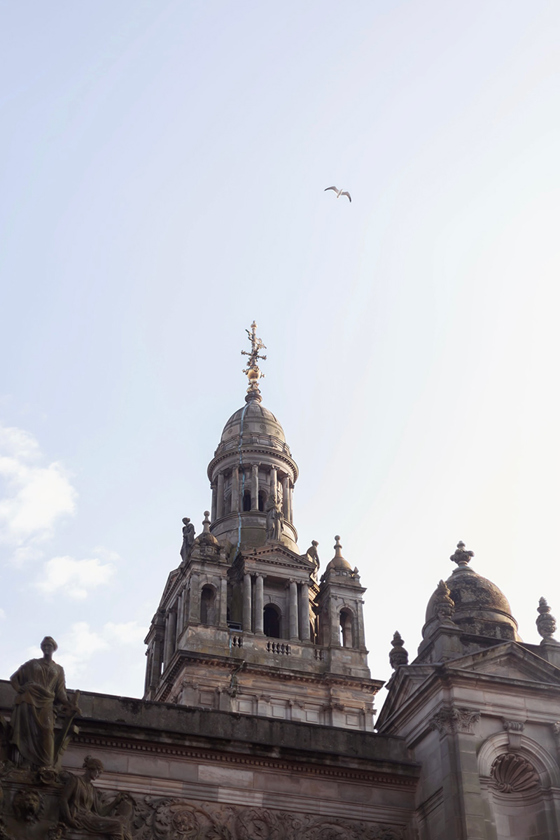 External shot of The Collector's Hall's historic exterior, with gold spier and a bird flying overhead.