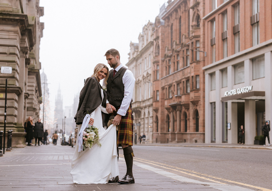 Bride and groom stand outside brand new wedding venue in Glasgow city centre, The Collector's Hall, with accommodation provider AC Hotel Glasgow in background.