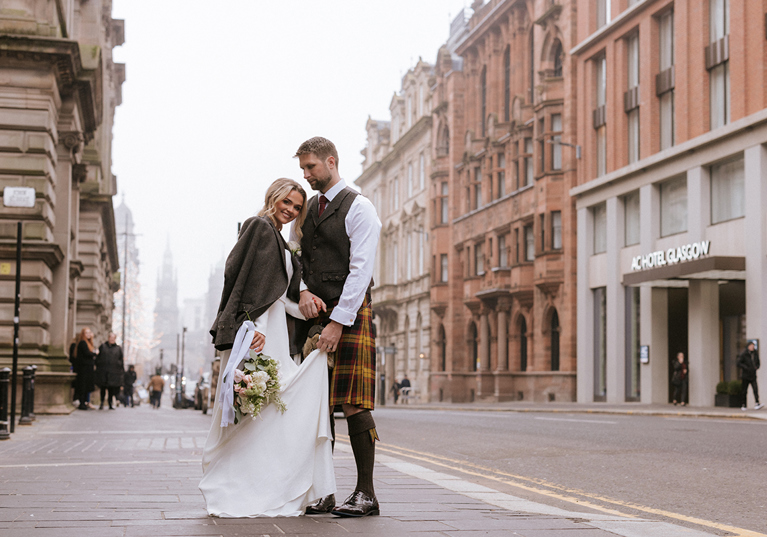 Bride and groom stand outside brand new wedding venue in Glasgow city centre, The Collector's Hall, with accommodation provider AC Hotel Glasgow in background.