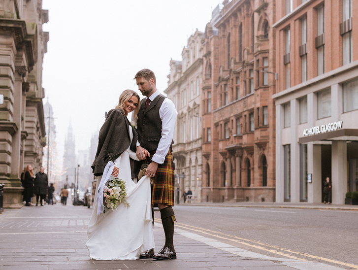 Bride and groom stand outside brand new wedding venue in Glasgow city centre, The Collector's Hall, with accommodation provider AC Hotel Glasgow in background.