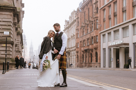 Bride and groom stand outside brand new wedding venue in Glasgow city centre, The Collector's Hall, with accommodation provider AC Hotel Glasgow in background.