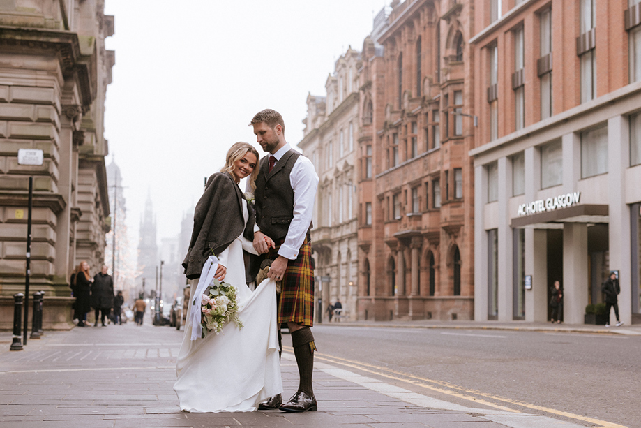 Bride and groom stand outside brand new wedding venue in Glasgow city centre, The Collector's Hall, with accommodation provider AC Hotel Glasgow in background.