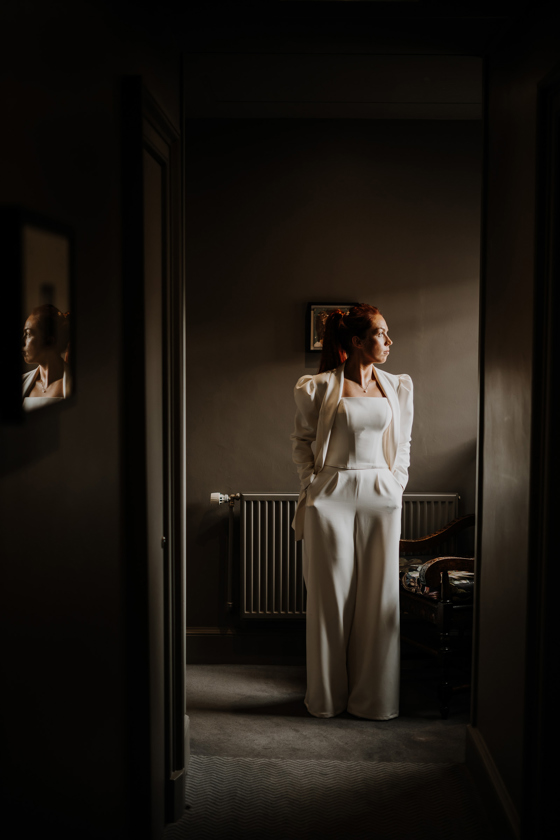 Bride wearing suit poses with her hands in her pockets.