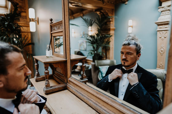 Groom fixes his bowtie in the mirror at The Scott Hotel.