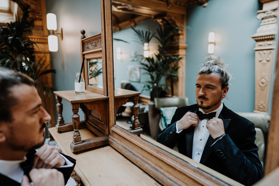 Groom fixes his bowtie in the mirror at The Scott Hotel.