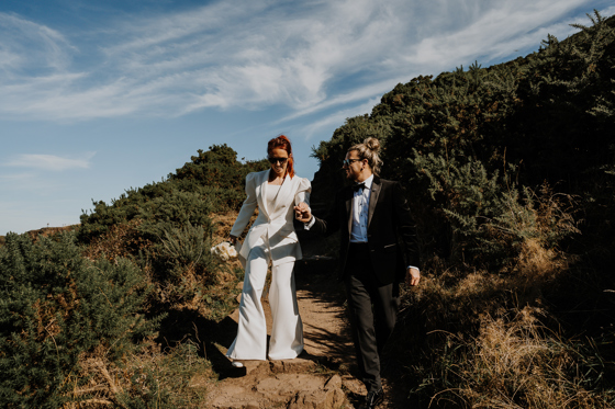 Newlyweds walking down sandy hill towards waterfront at The Scott Hotel in Edinburgh.