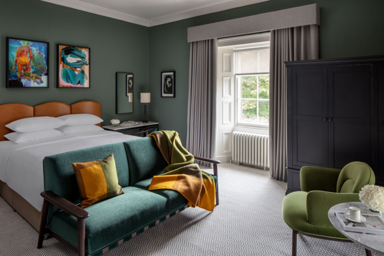 Bedroom at The Scott Hotel in Edinburgh, showing colourful elements such as a teal sofa and green chair, with colourful artwork on wall behind bed.